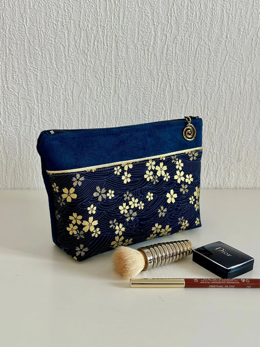 La pochette à maquillage fleurie bleu et dorée, présentée avec des pinceaux et stylos à lèvre.