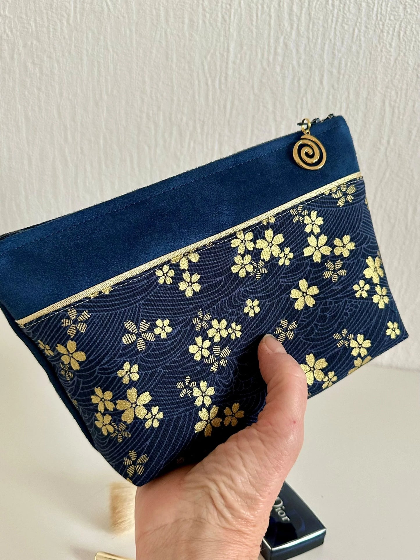 La pochette à maquillage fleurie bleu et dorée, tenue dans la main.
