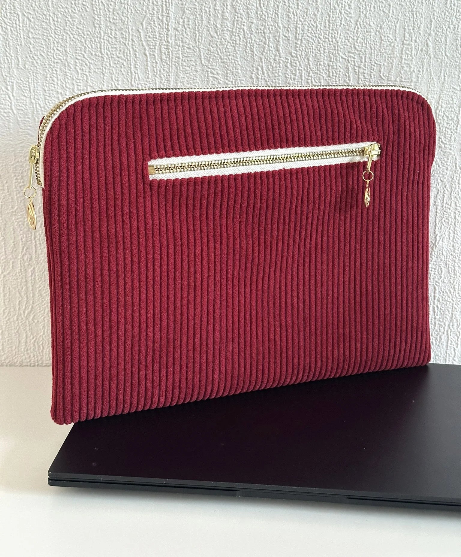Face arrière de la pochette ordinateur en velours cotelé bordeaux avec la poche zippée pour le chargeur.