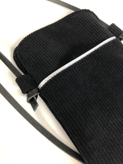 La poche avant de la pochette téléphone bandoulière en velours cotelé noir et cuir.