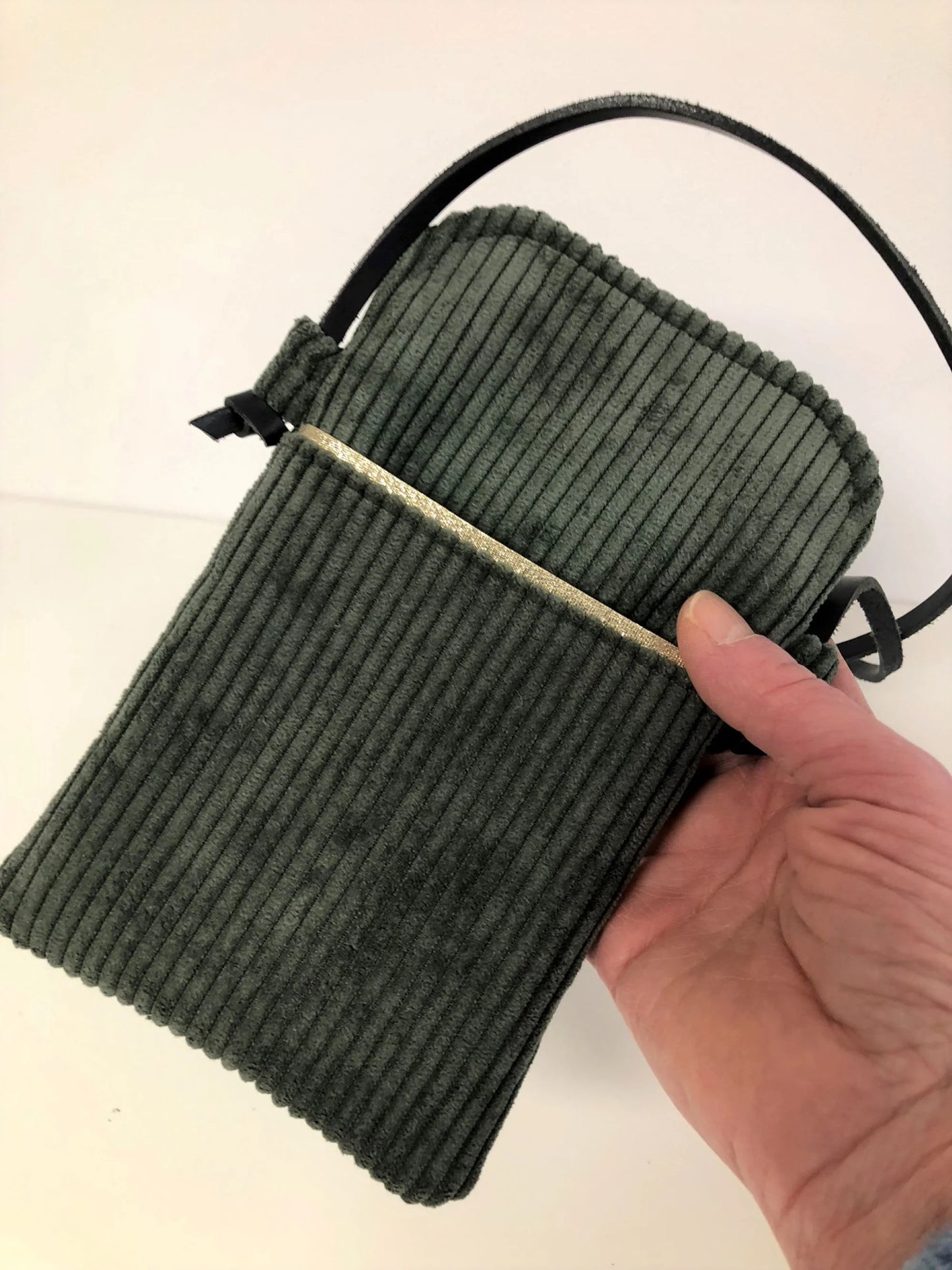 La pochette téléphone bandoulière en velours cotelé vert kaki , tenue en main.