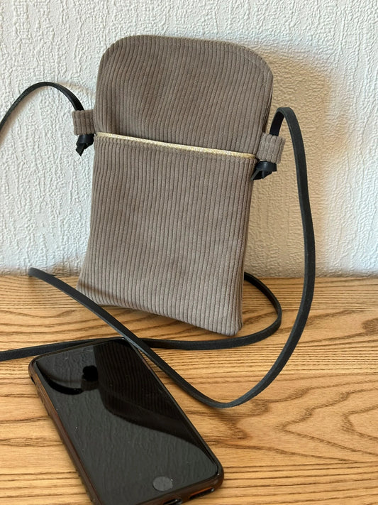 La pochette téléphone en velours cotelé taupe et lanière en cuir noir nouée.