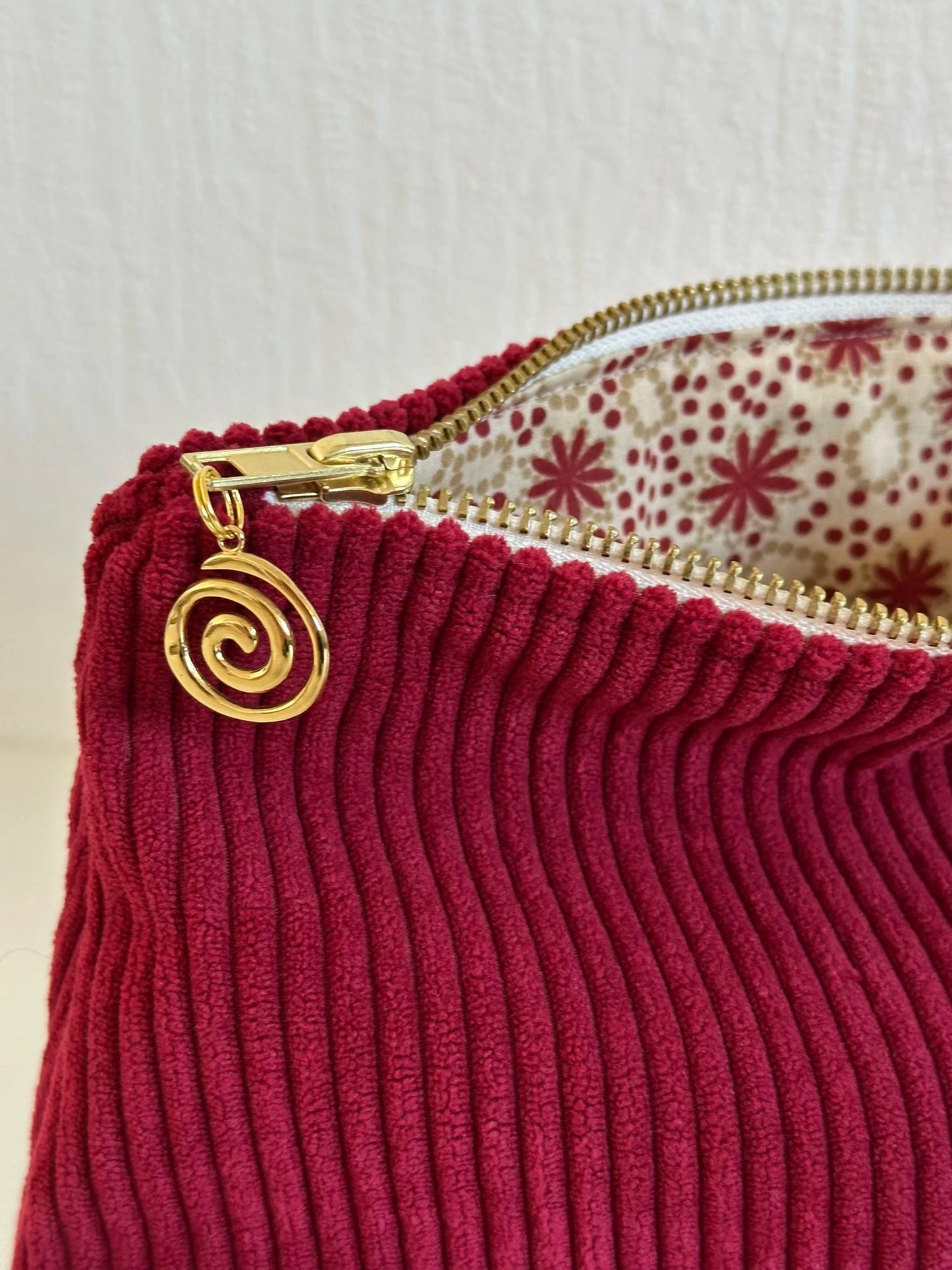 Détail de la fermeture éclair dorée de la pochette en velours cotelé bordeaux.