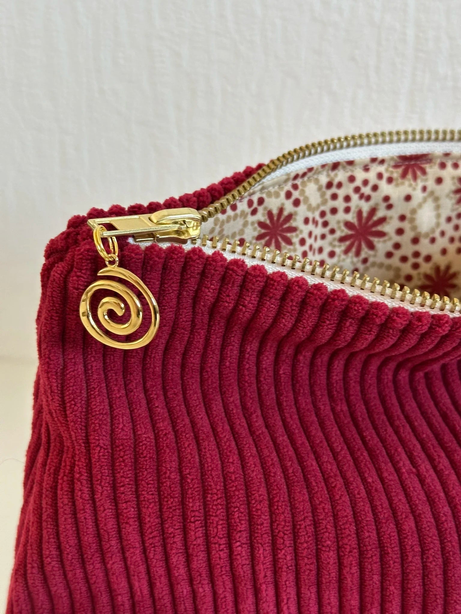Détail de la fermeture éclair dorée de la pochette en velours cotelé bordeaux.
