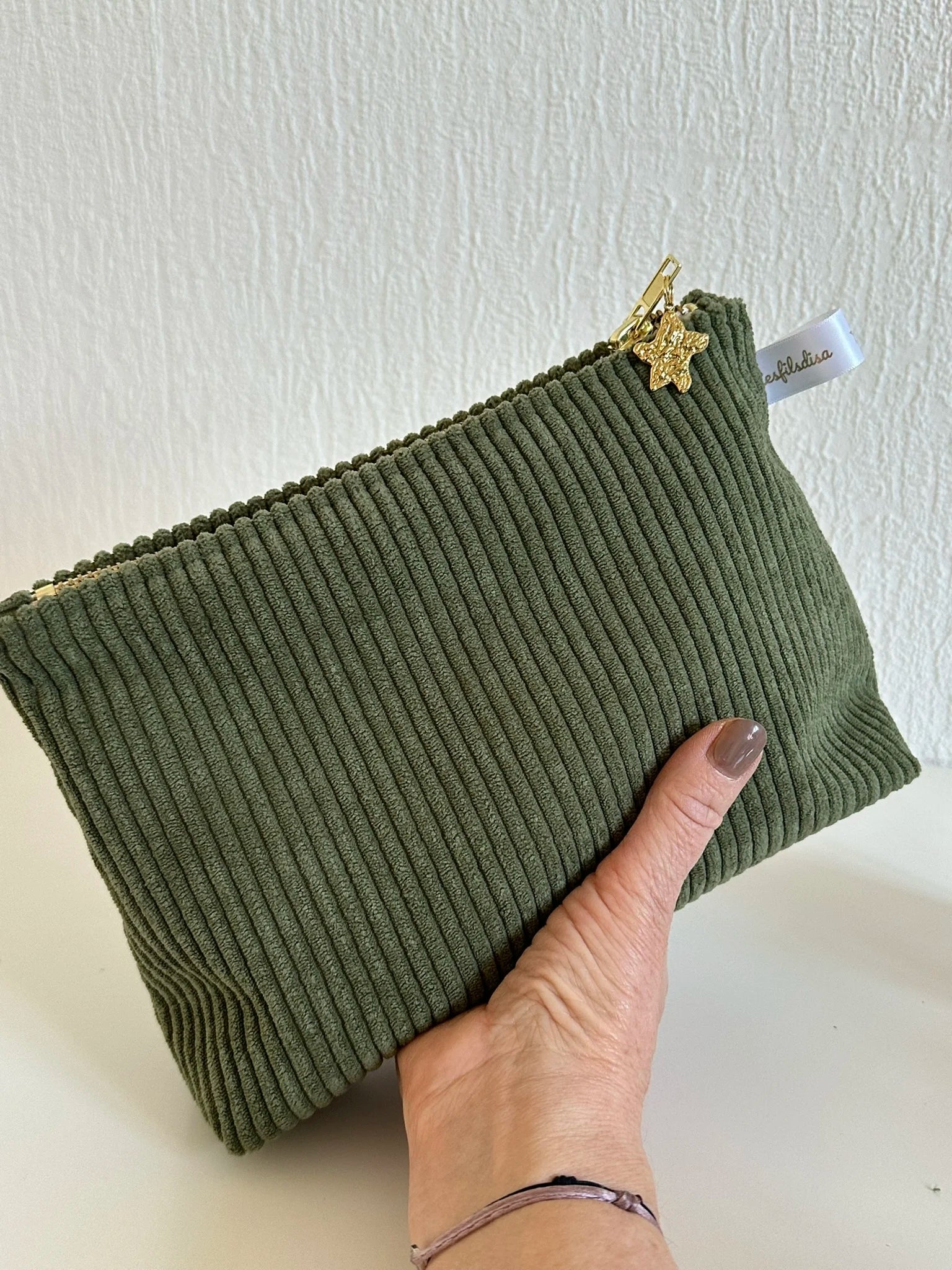 La pochette en velours côtelé vert armée, tenue dans la main.