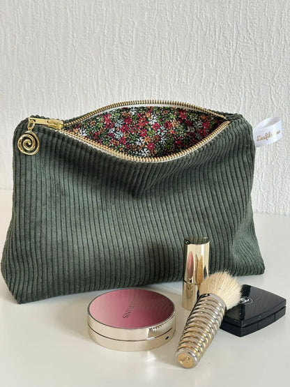La pochette en velours côtelé vert kaki,  ouverte et présentée avec des accessoires de maquillage ( non fournis).