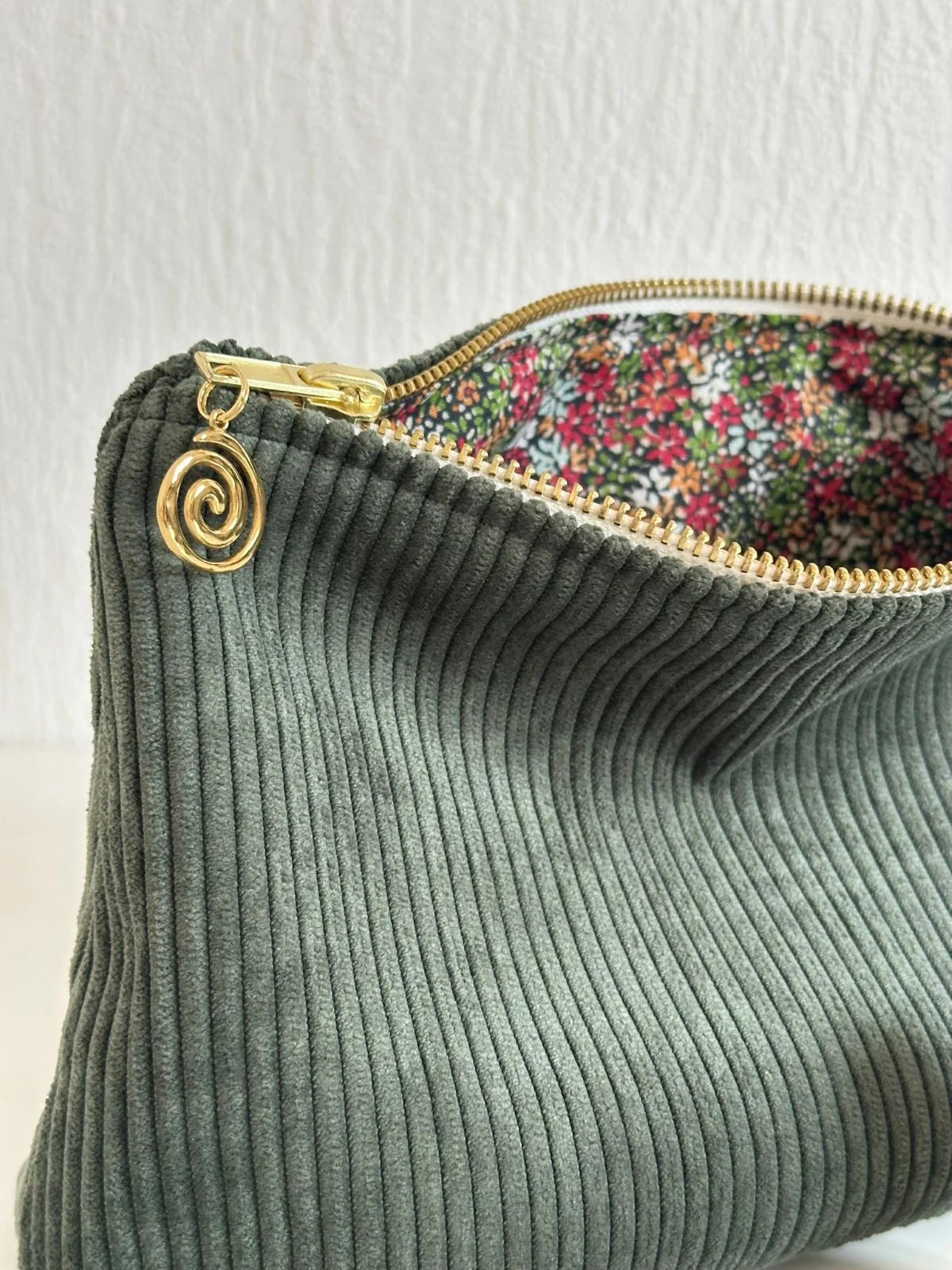 La breloque dorée de la pochette en velours côtelé vert kaki.