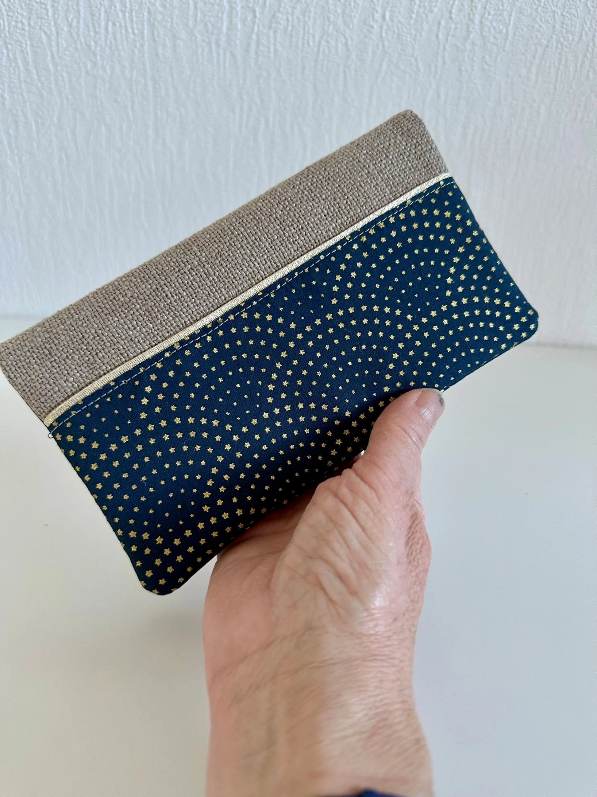 Le porte chéquier beige et bleu à étoiles dorées, tenu dans la main.