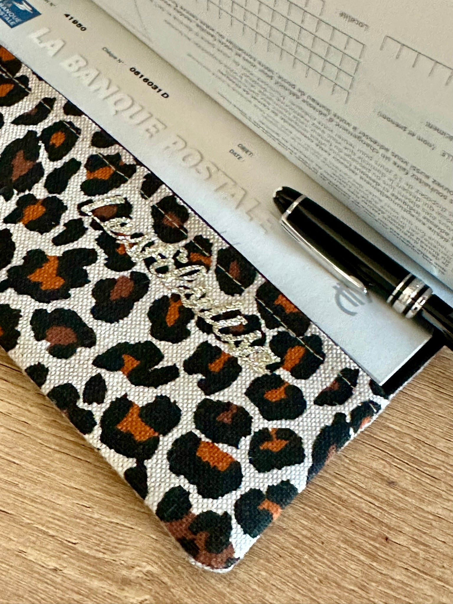 Le rabat inférieur du porte-chéquier léopard en lin beige.