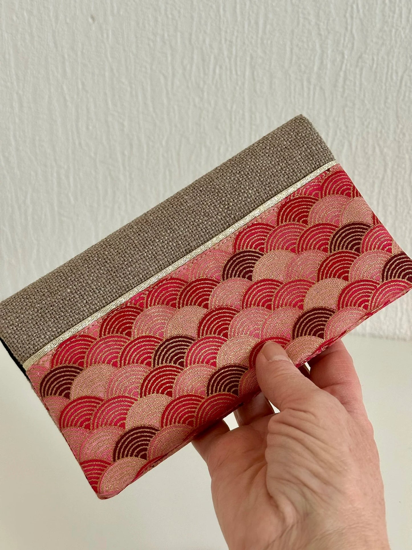 Le porte chéquier en lin et tissu japonais rose et rouge, tenu dans la main.