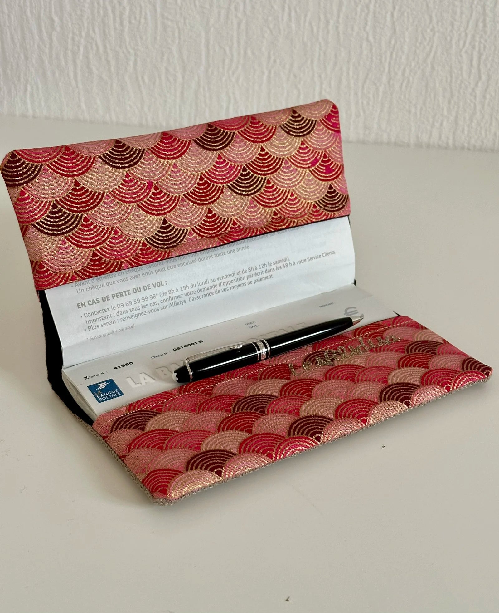 Le porte chéquier en lin et tissu japonais rose et rouge, ouvert avec un carnet de chèques à l'intérieur.
