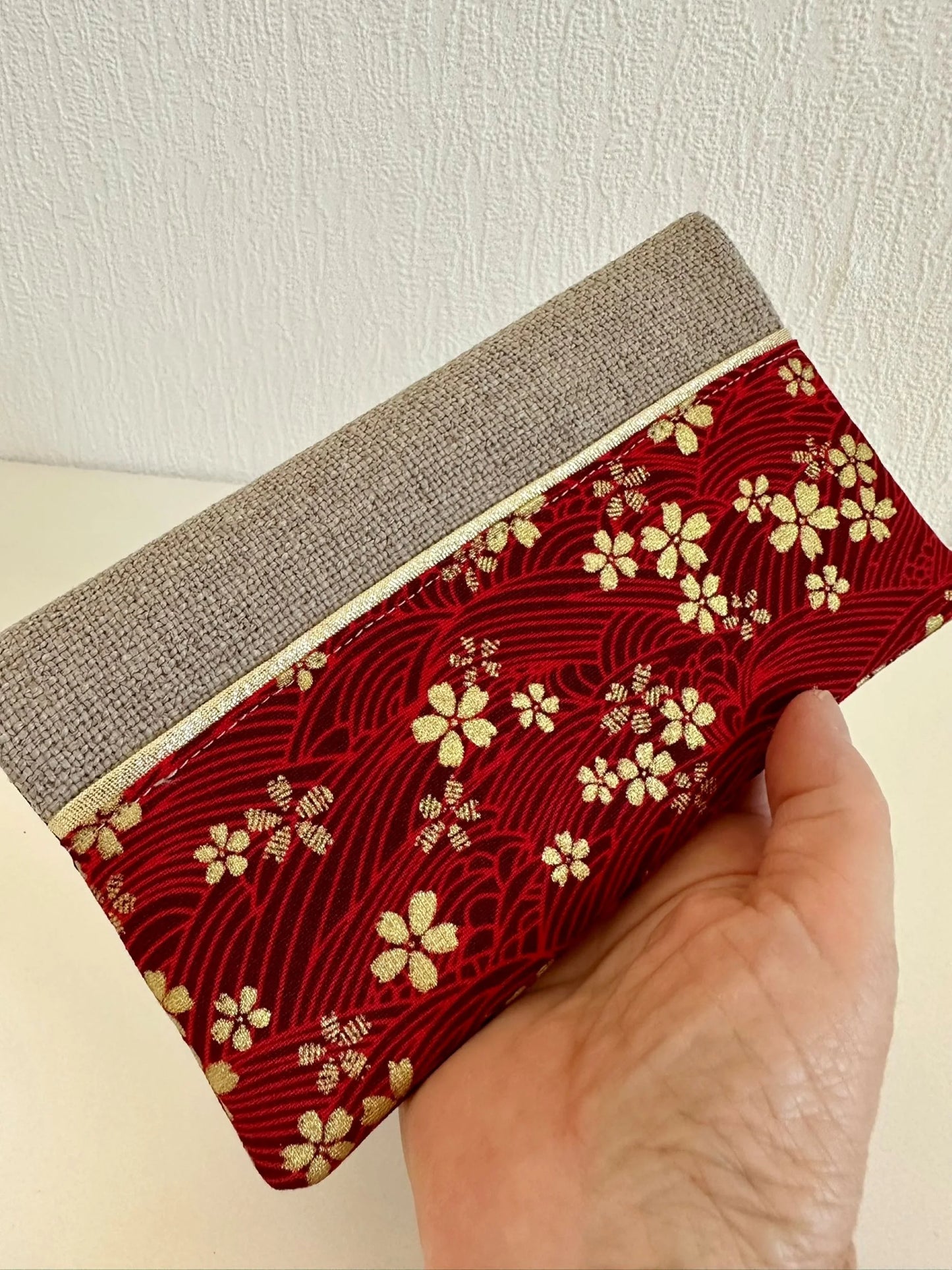 Le porte chéquier en lin et tissu japonais sakura rouge et doré, tenu dans la main.