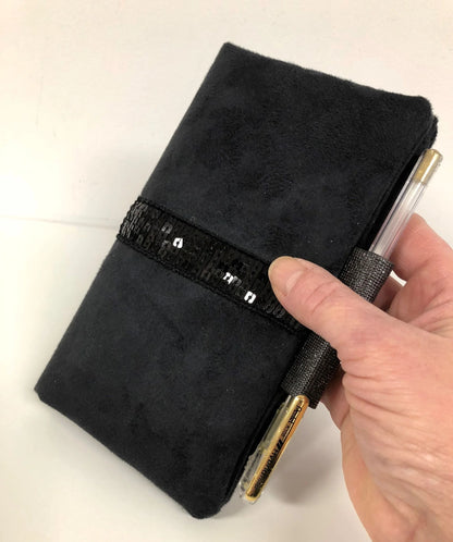 le porte chéquier noir à paillettes avec porte stylo, tenu en main.