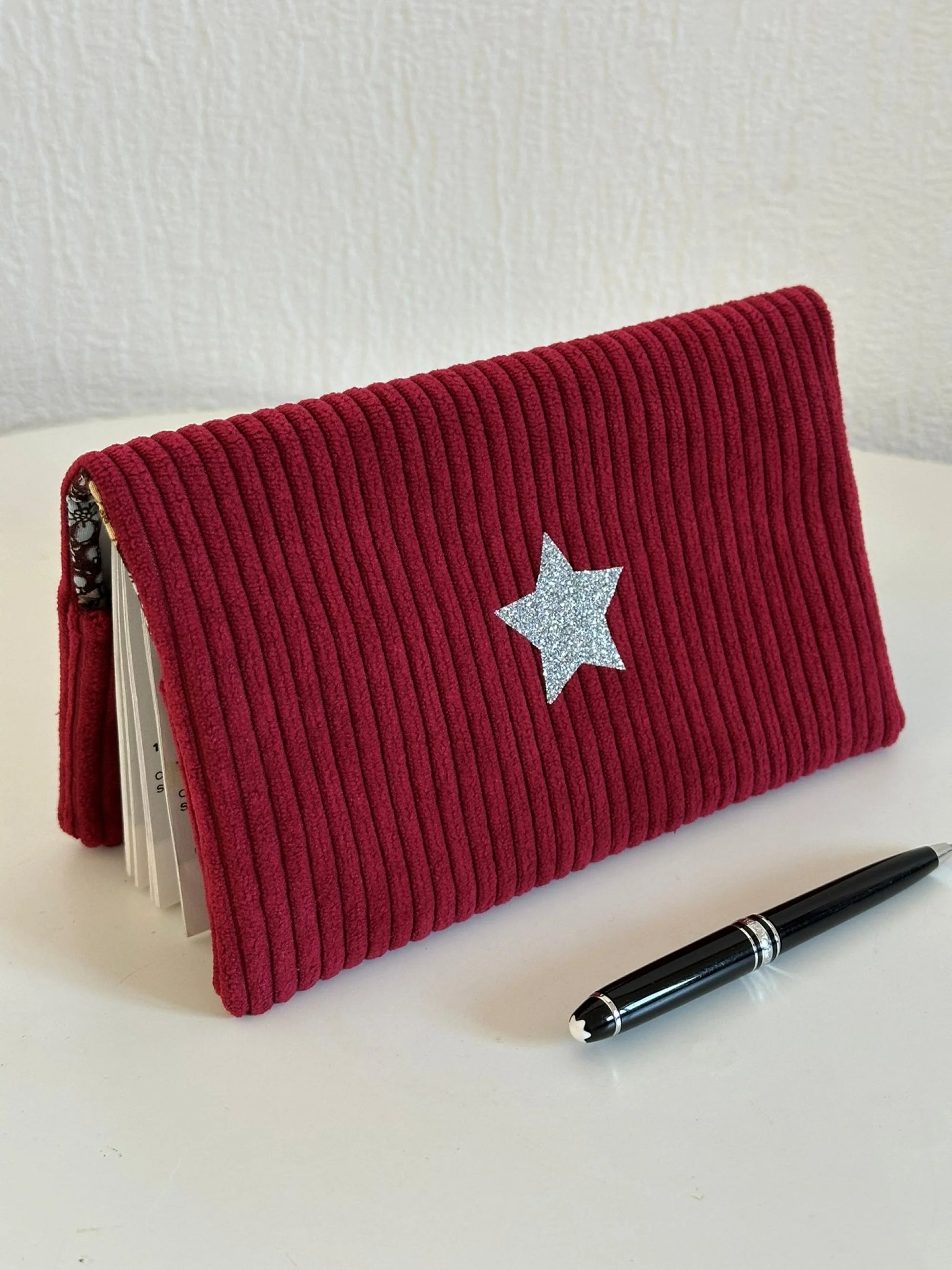 Le porte chéquier en velours bordeaux avec étoile pailletée argentée en face avant.