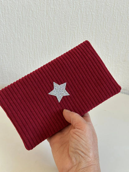 Le porte chéquier en velours bordeaux avec étoile pailletée , tenu dans la main.