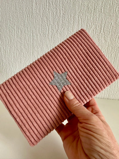 Le porte chéquier en velours rose blush tenu dans la main.