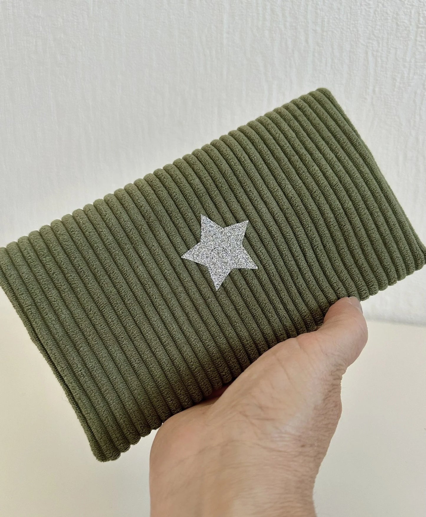Le porte chéquier en velours vert armée et son étoile pailletée argentée  tenu en main.