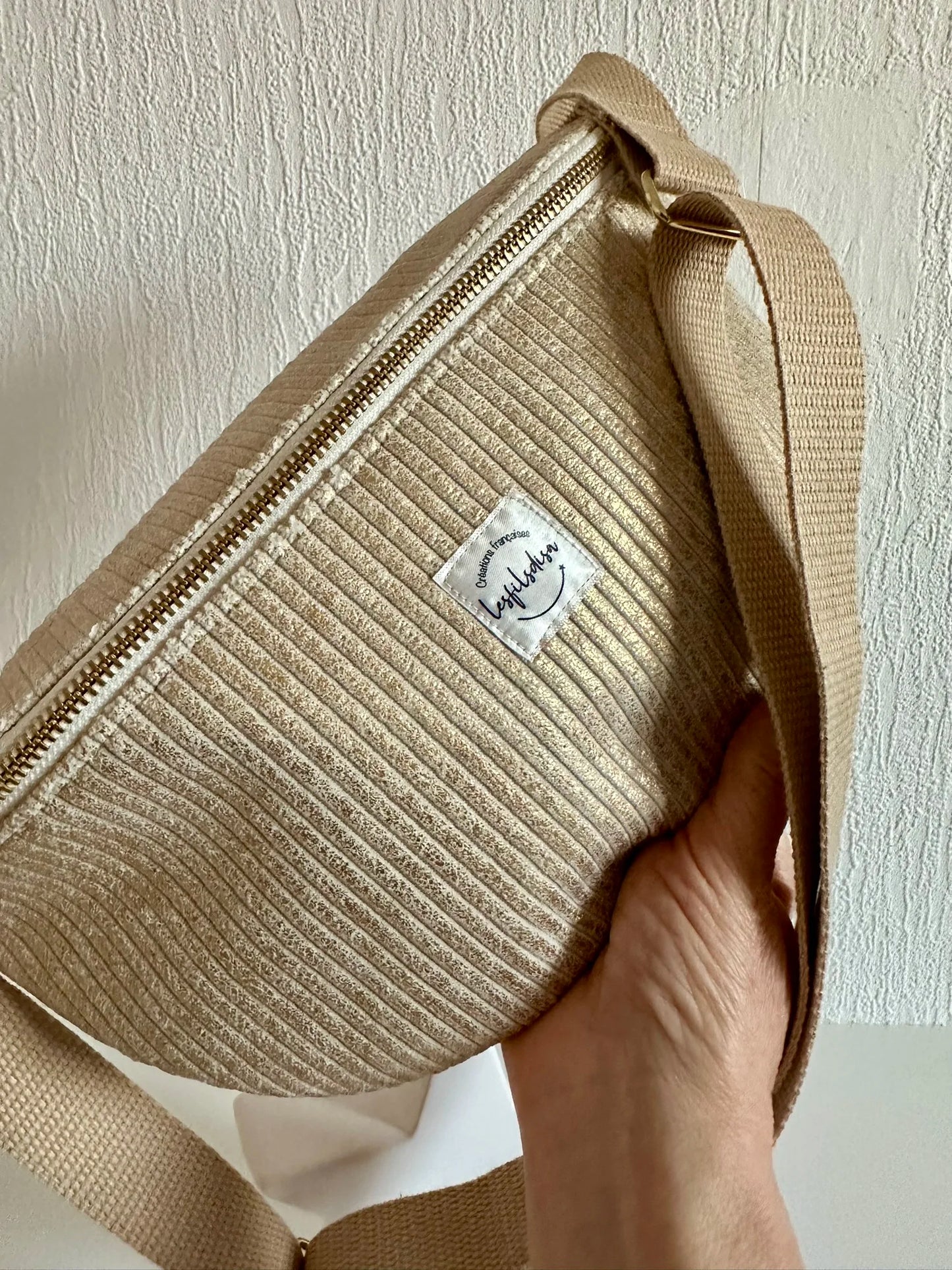 Le sac banane en velours cotelé doré tenu dans la main.