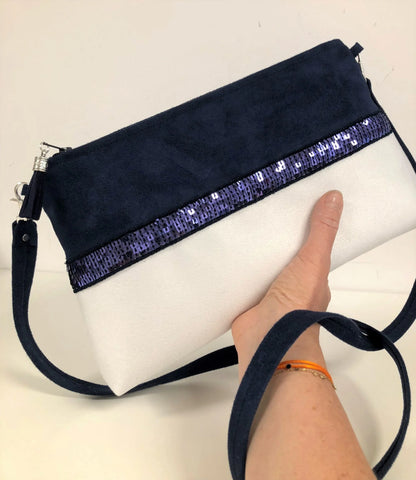 Le sac bandoulière Isa bleu marine et blanc à paillettes, tenu en main.