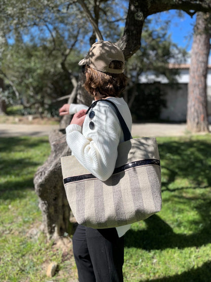 Le sac cabas Isa en lin à larges rayures et paillettes noires, porté à l'épaule.