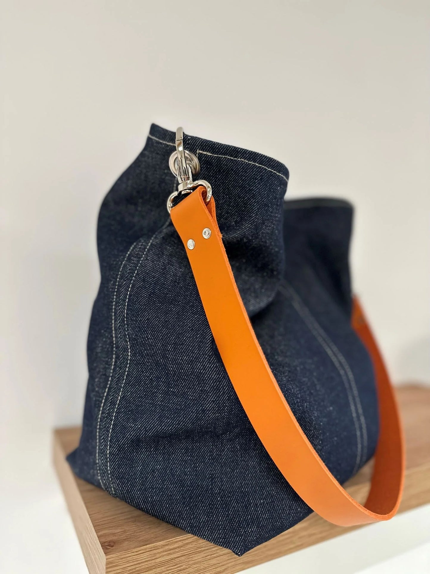 Vue d'ensemble du sac hobo en denim et son anse en cuir orange .