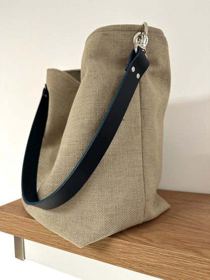 Vue d'ensemble du sac Hobo en lin beige et son anse en cuir bleu marine .