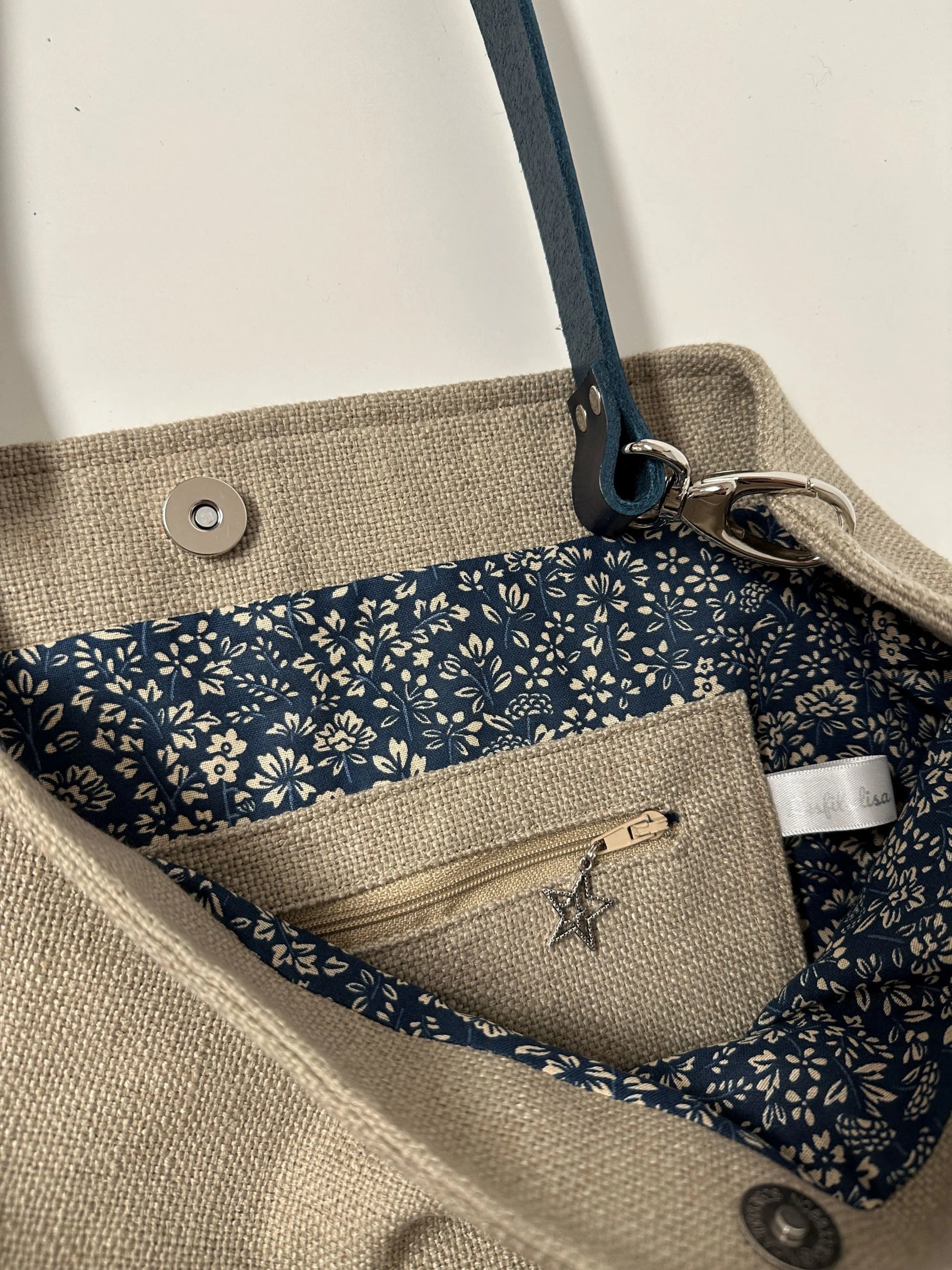 La poche intérieure zippée du sac Hobo en lin beige et son anse en cuir bleu marine .
