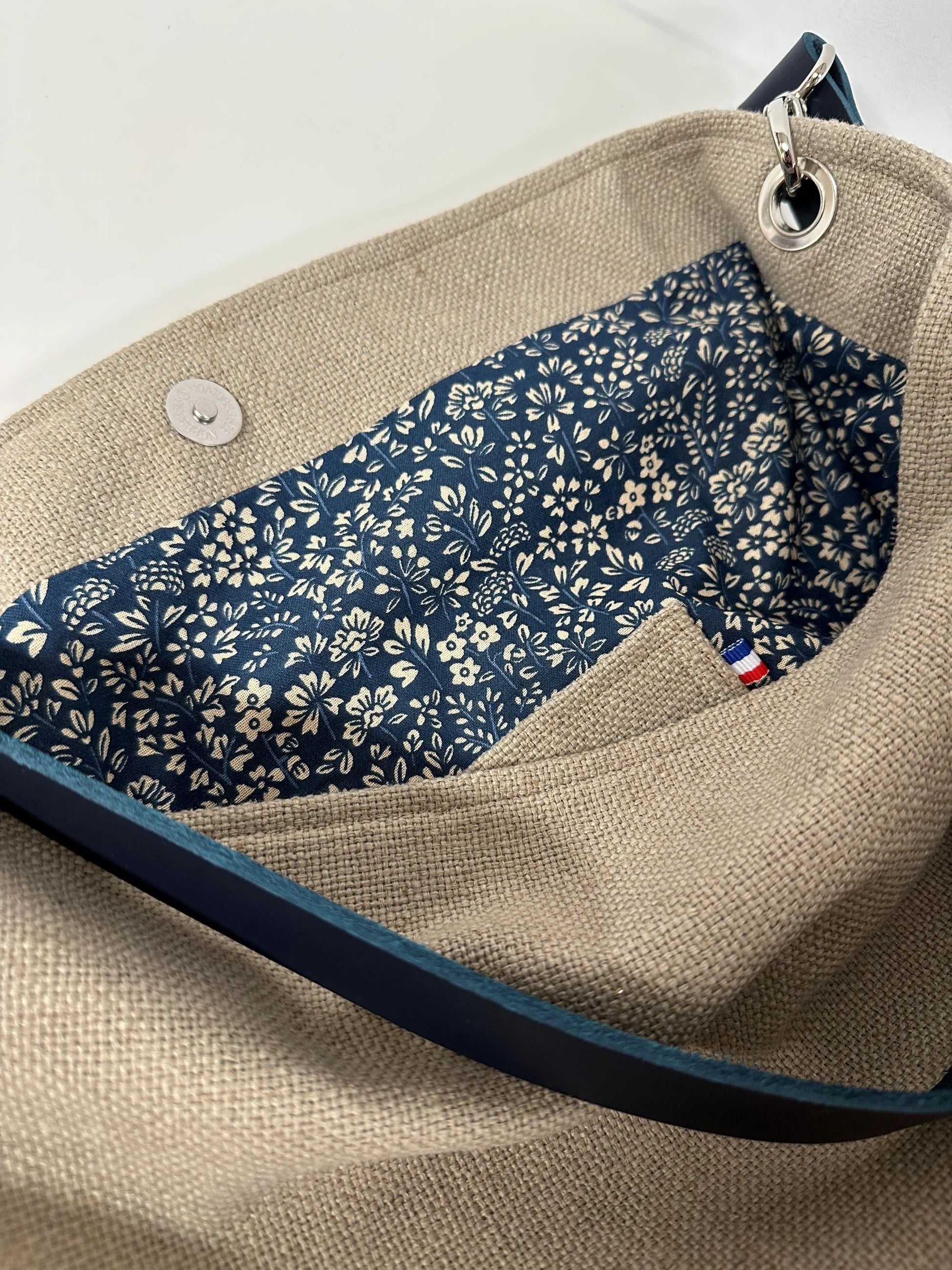 La poche plaquée intérieure du sac Hobo en lin beige et son anse en cuir bleu marine .