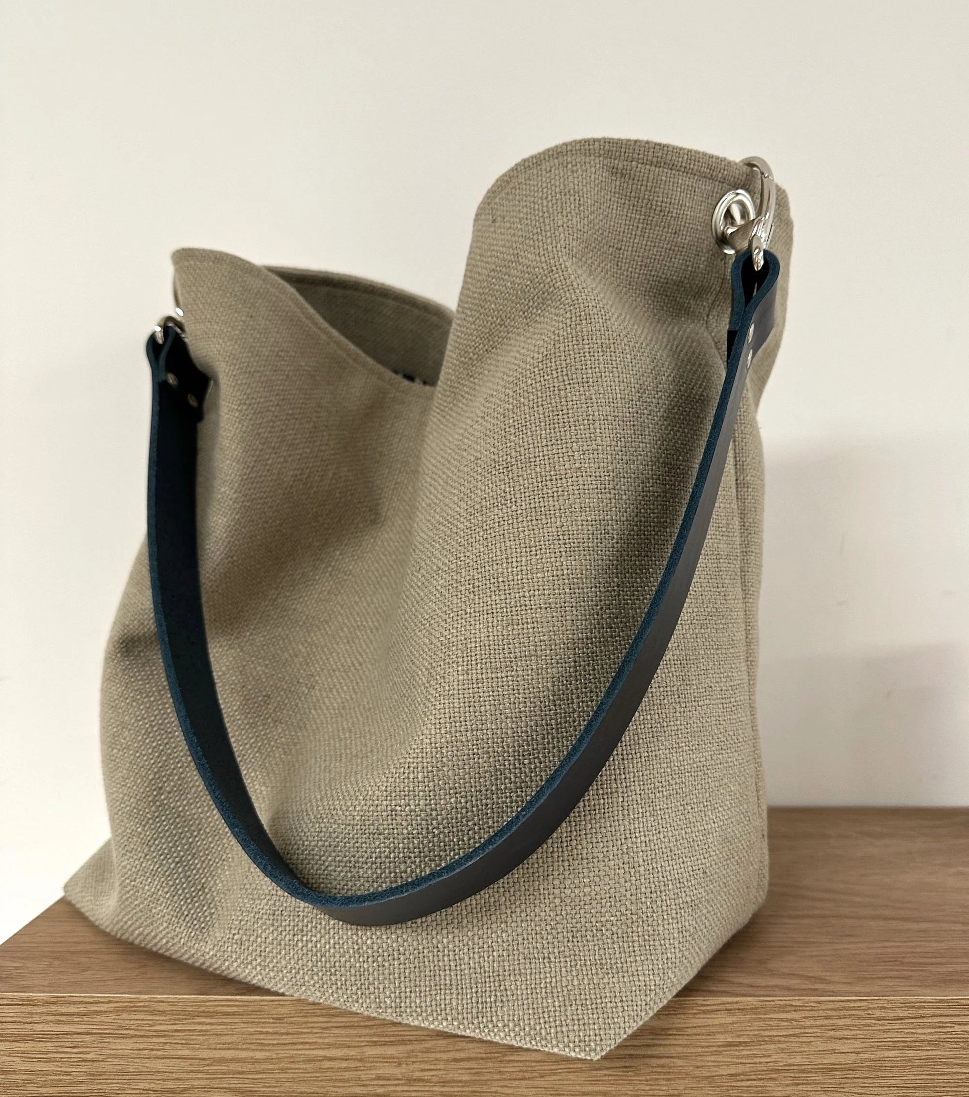 Le sac Hobo en lin beige et son anse en cuir bleu marine amovible.