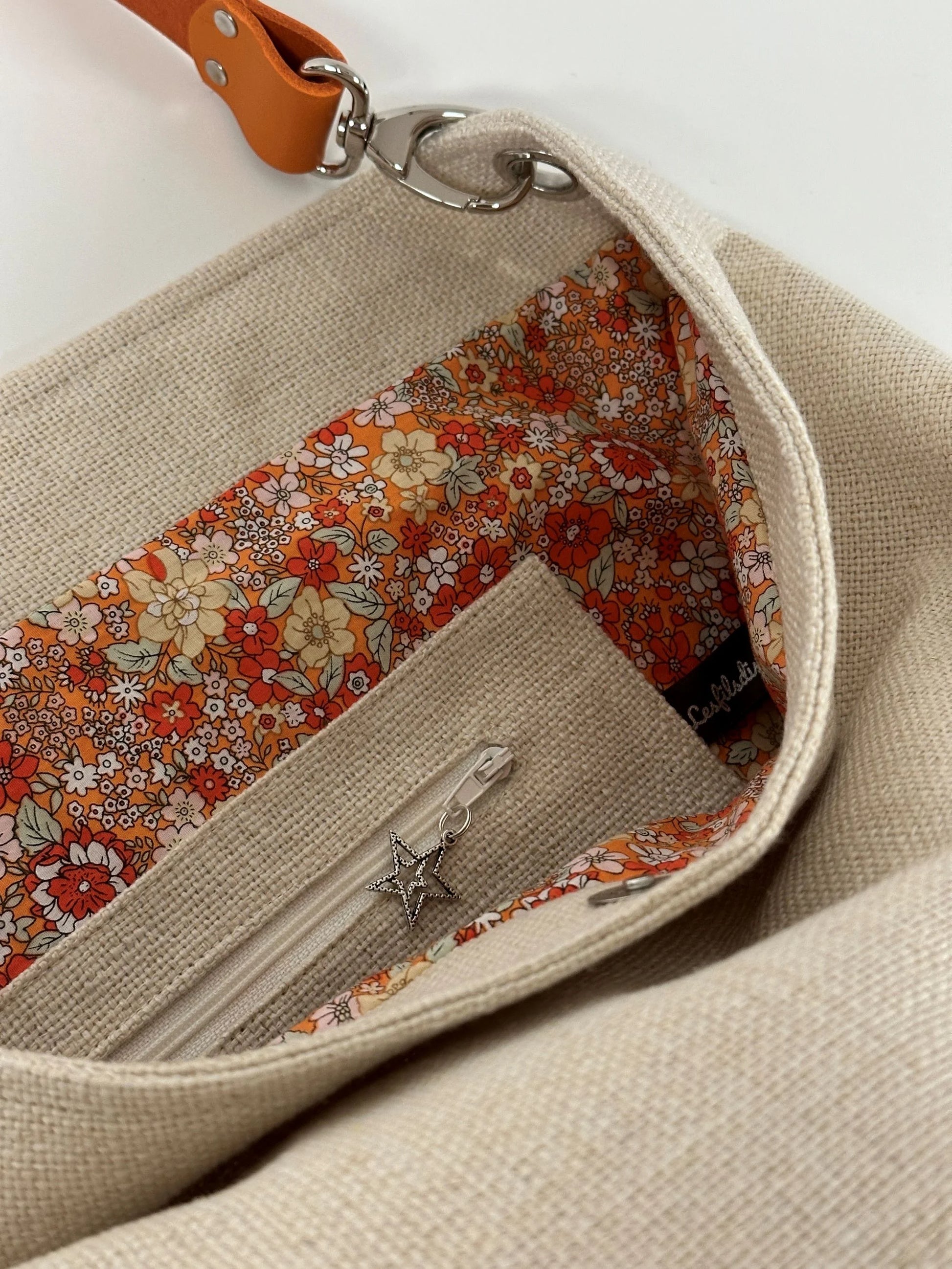 La poche intérieure zippée du sac hobo en lin ivoire et son anse en cuir orange.