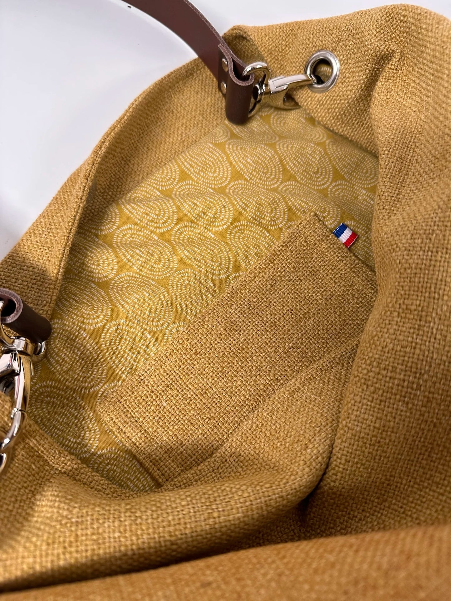 La poche intérieure plaquée du sac hobo en lin jaune moutarde et son anse en cuir marron amovible.