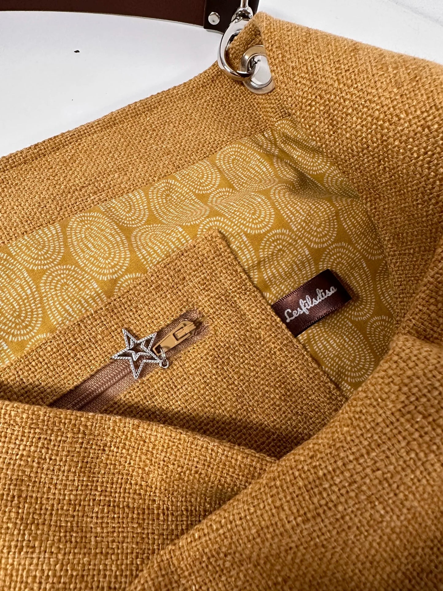 La poche zippée intérieure du sac hobo en lin jaune moutarde et son anse en cuir marron amovible.
