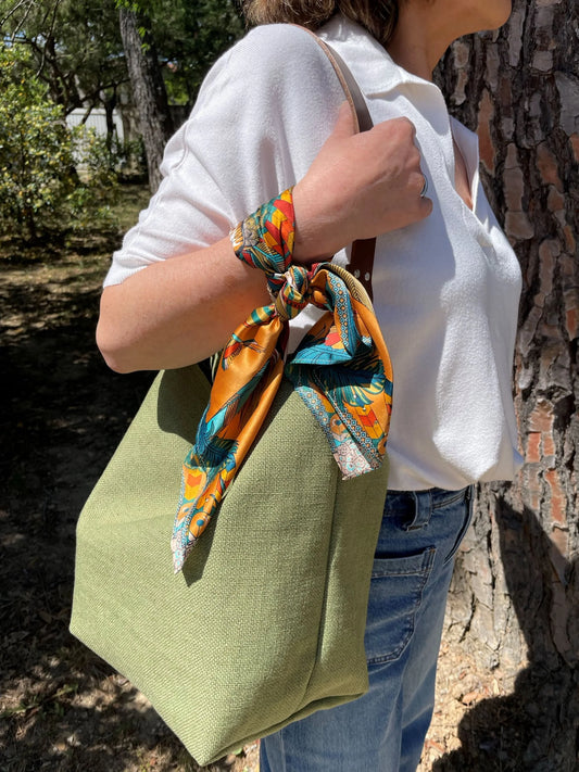 Le sac hobo en lin vert kaki et son anse en cuir marron amovible, porté à l'épaule.