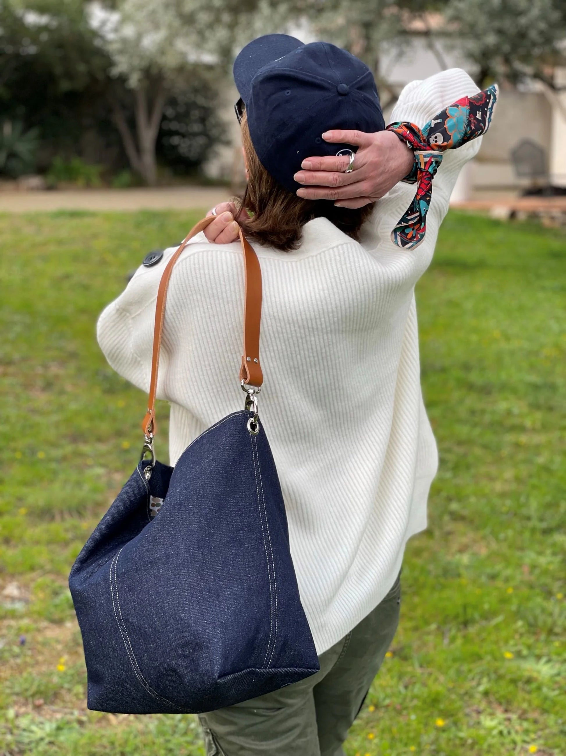 Le sac hobo en toile denim brut et son anse en cuir fauve porté à l'épaule.