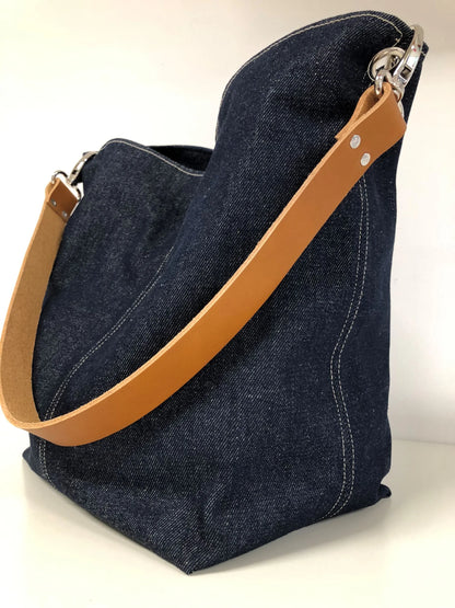 Le sac hobo en toile denim brut et son anse en cuir fauve.