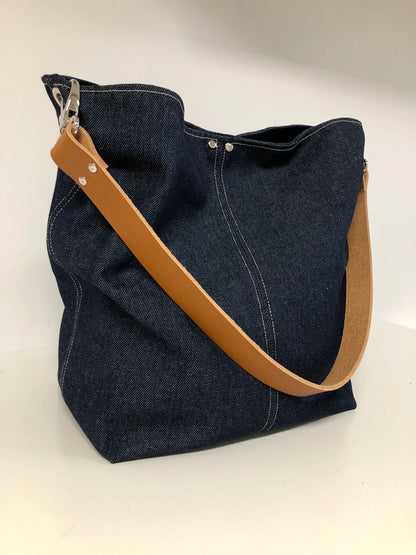 Les surpiqures du sac hobo en toile denim brut et son anse en cuir fauve.