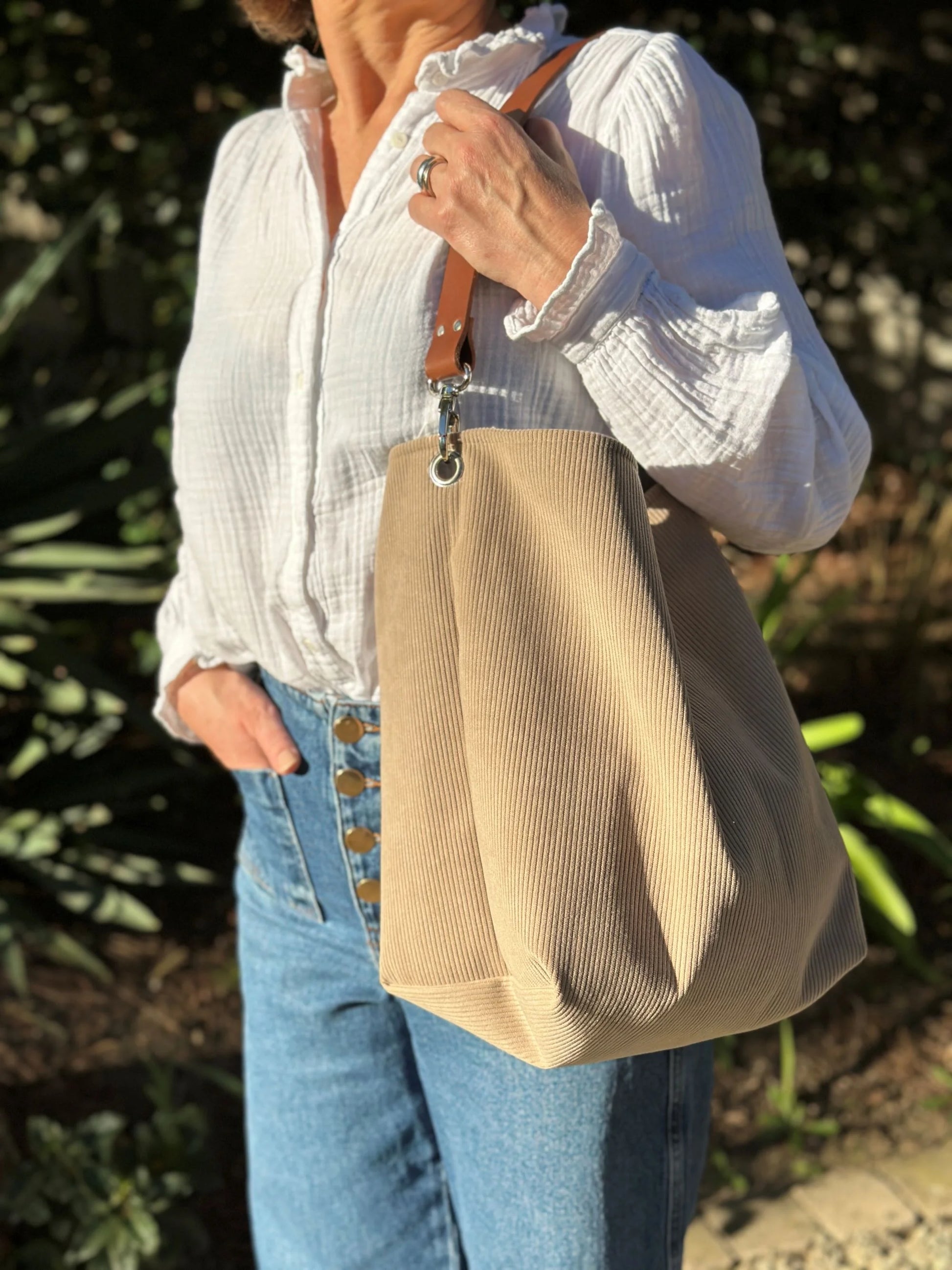 Le sac hobo en velours cotelé beige et son anse en cuir marron, porté à l'épaule.