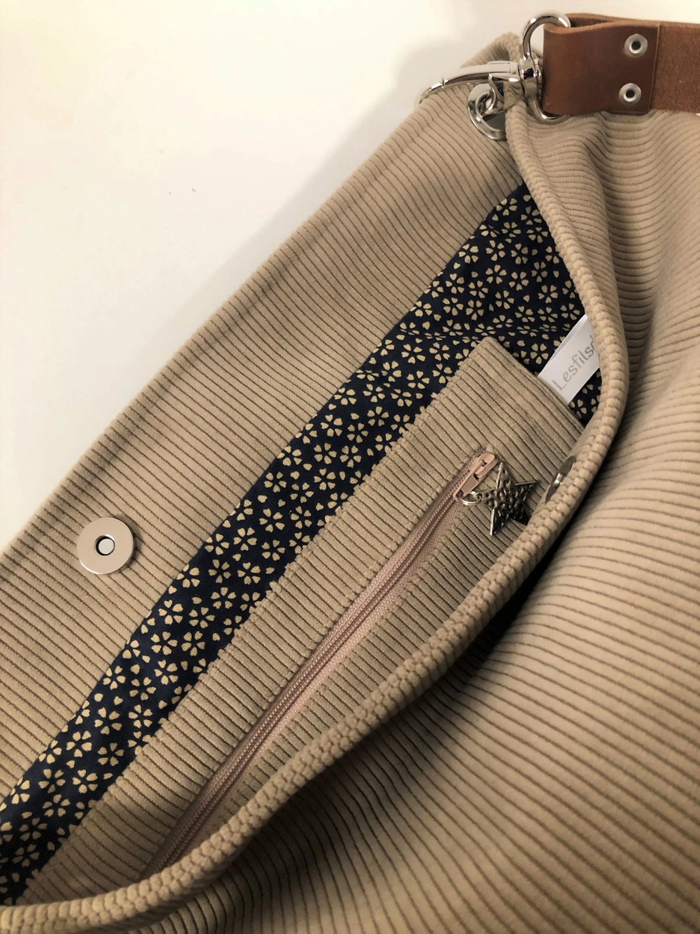 La poche intérieure zippée du sac hobo en velours cotelé beige et son anse en cuir marron.