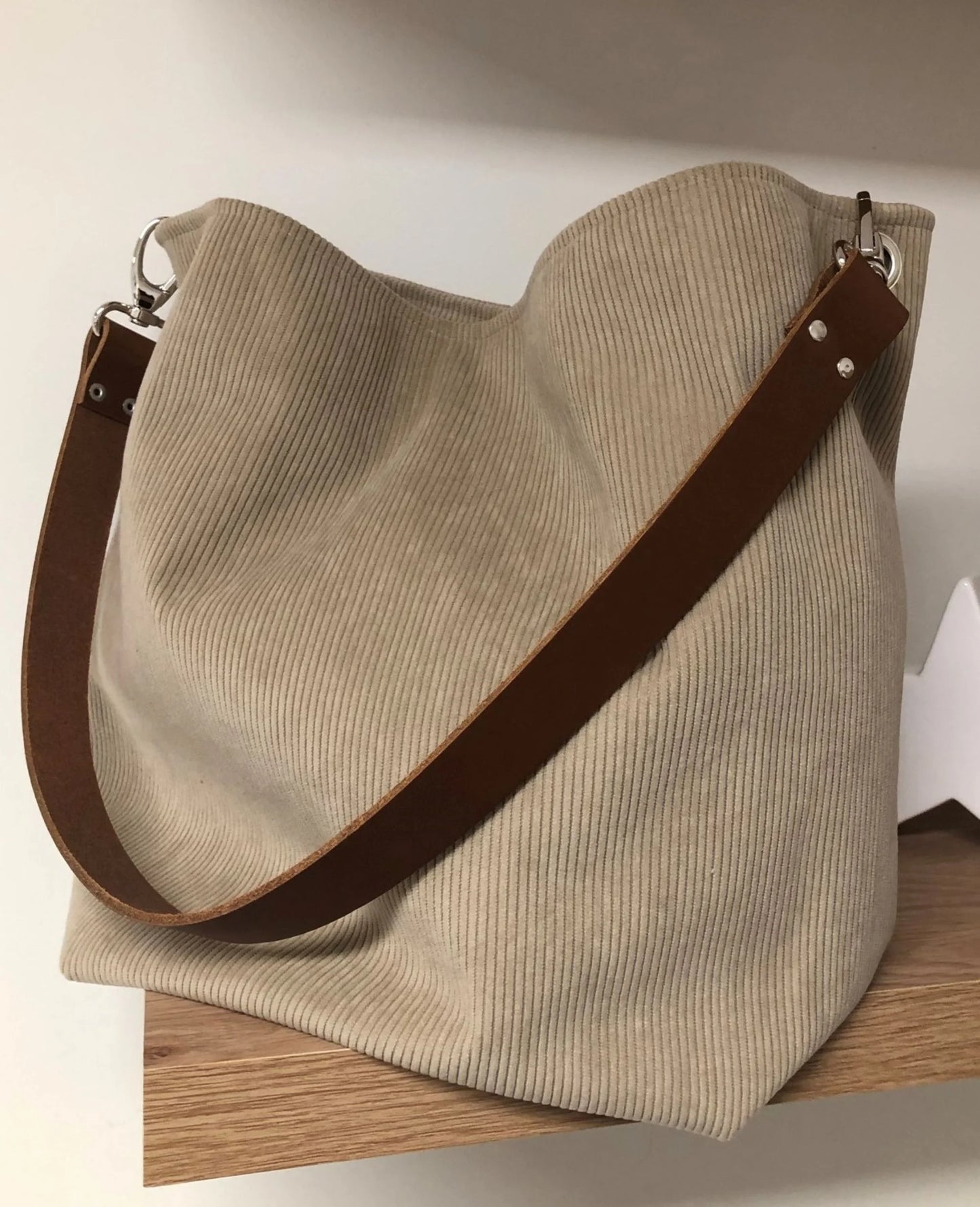 Vue d'ensemble du sac hobo en velours cotelé beige et son anse en cuir marron.