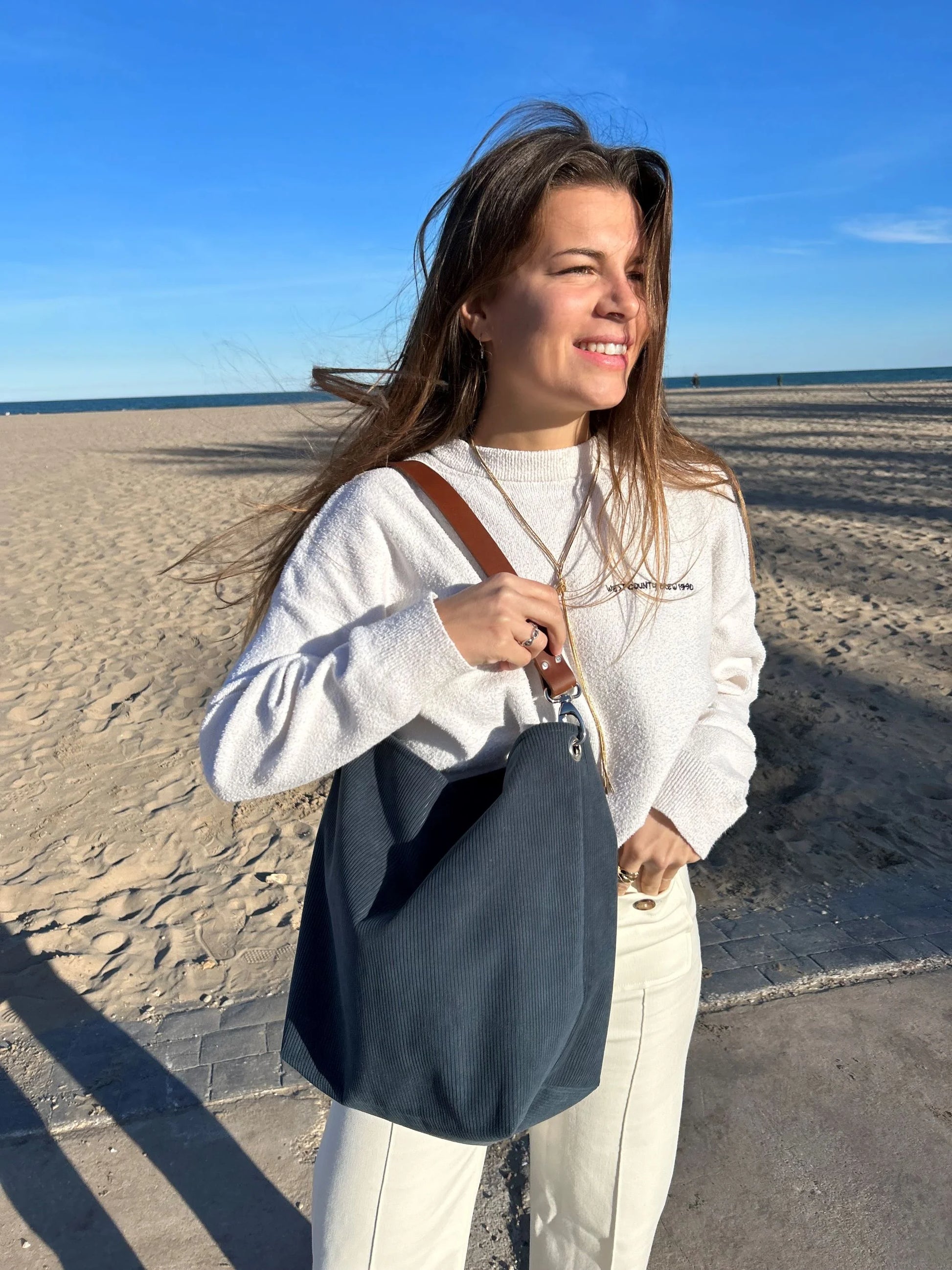 Le sac hobo en velours cotelé bleu canard et son anse en cuir marron porté à l'épaule.