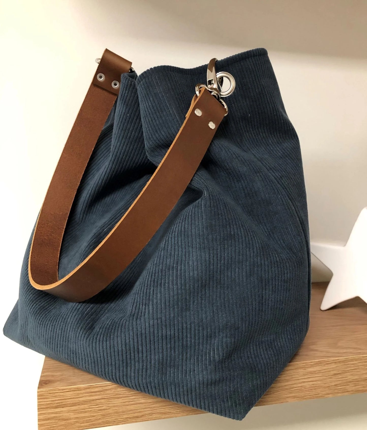 Le sac hobo en velours cotelé bleu canard et son anse en cuir marron amovible.