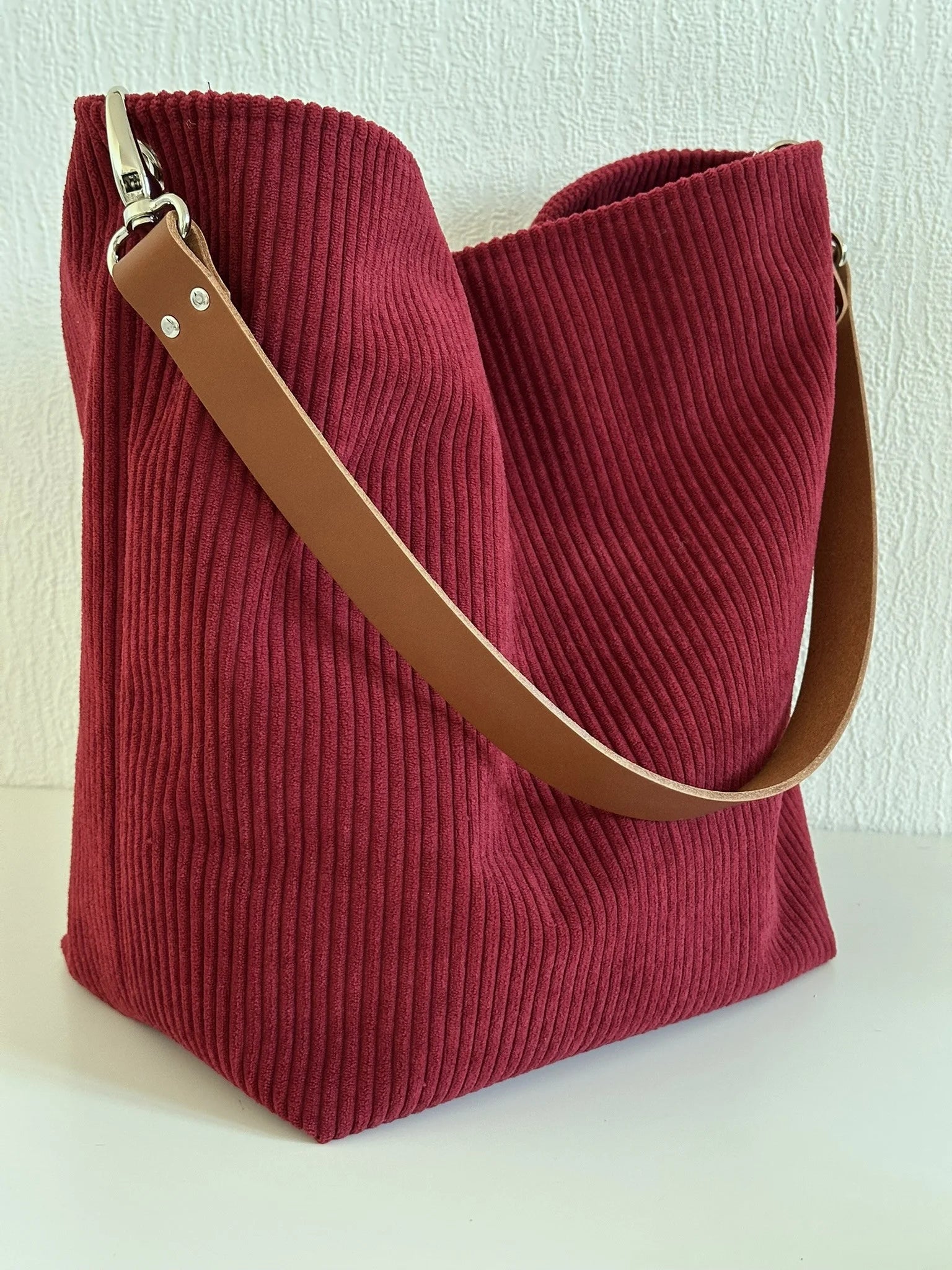 Le sac Hobo en velours cotelé bordeaux, et anse en cuir fauve.