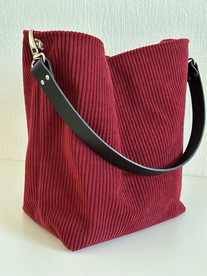 Vue d'ensemble du sac Hobo en velours cotelé bordeaux, et anse en cuir noir.