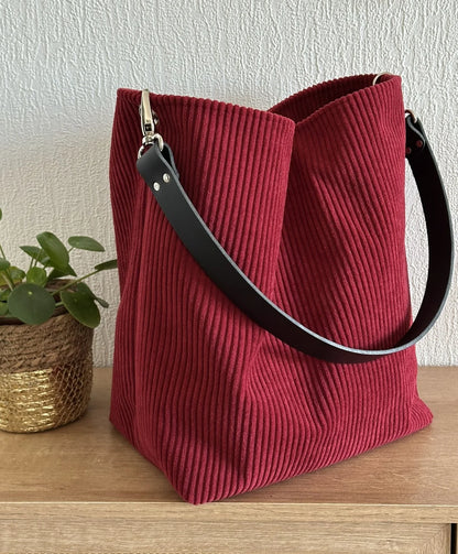 Le sac Hobo en velours cotelé bordeaux, et anse en cuir noir.