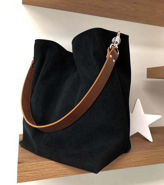 Le sac hobo en velours cotelé noir et son anse en cuir marron.