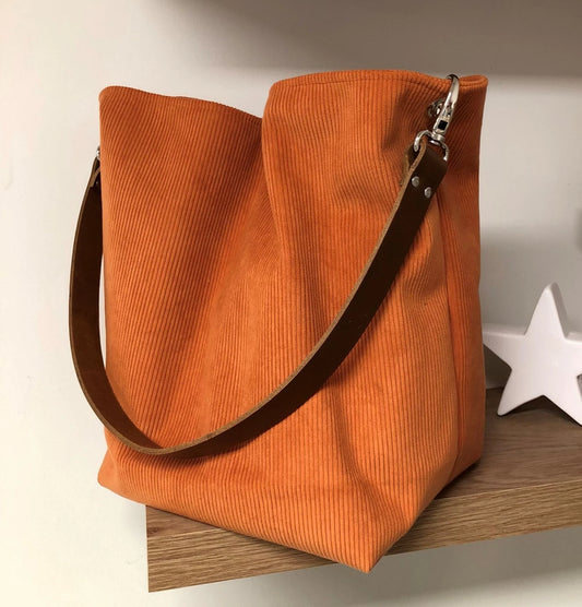 Le sac hobo en velours cotelé orange et son anse en cuir marron.