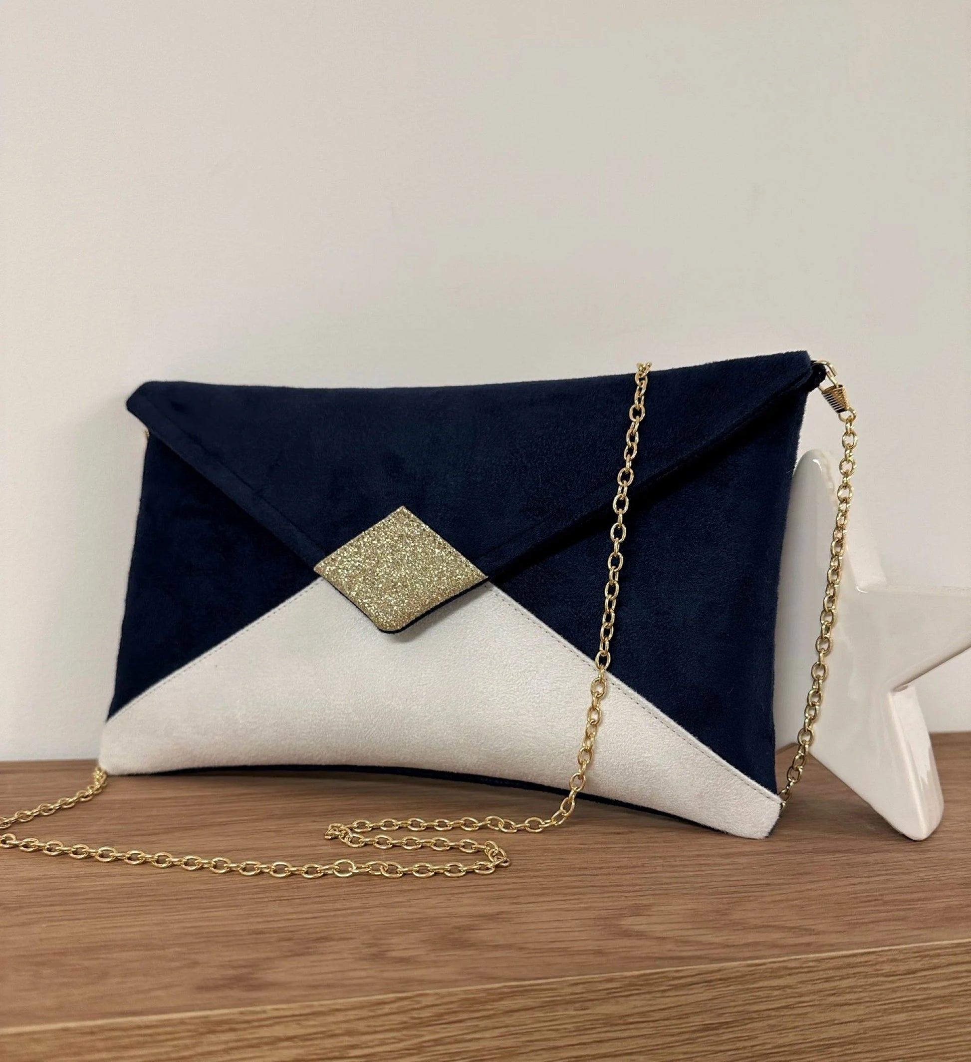 Le sac pochette Isa bleu marine et blanc à paillettes dorées, avec chainette amovible.