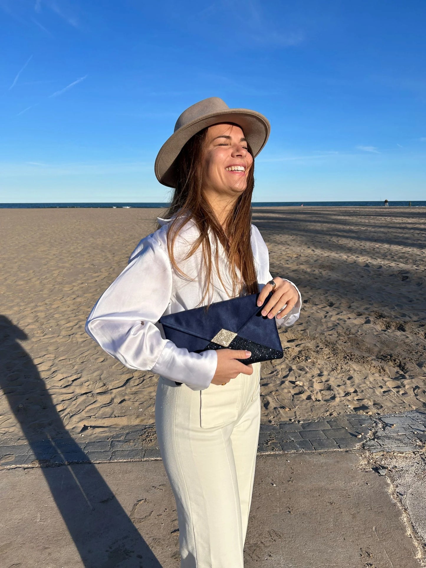 Le sac pochette Isa bleu marine et doré à paillettes, avec chainette amovible, porté par jeune femme.