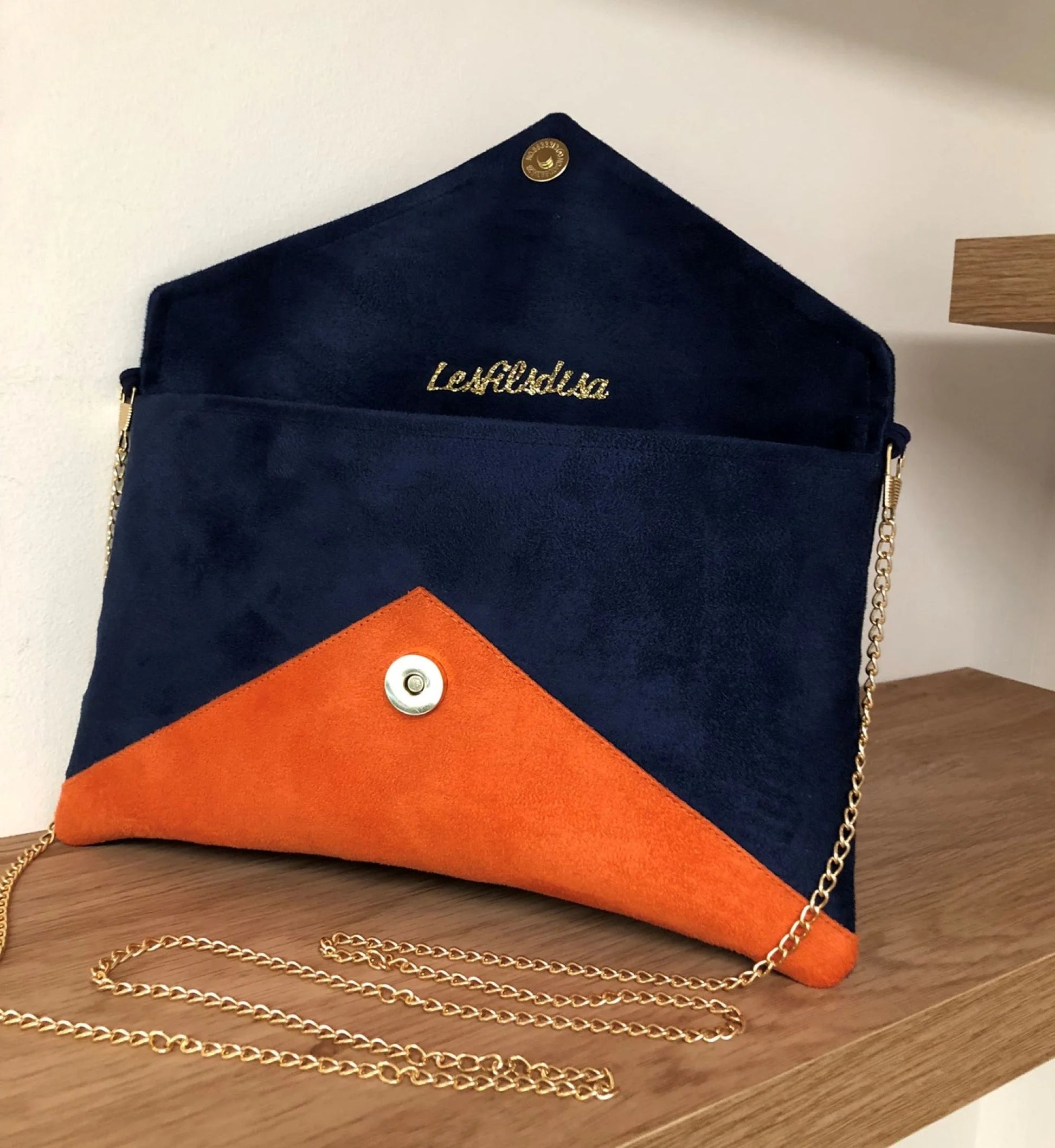 le sac pochette Isa bleu marine et orange à paillettes dorées, ouvert, avec chainette amovible.