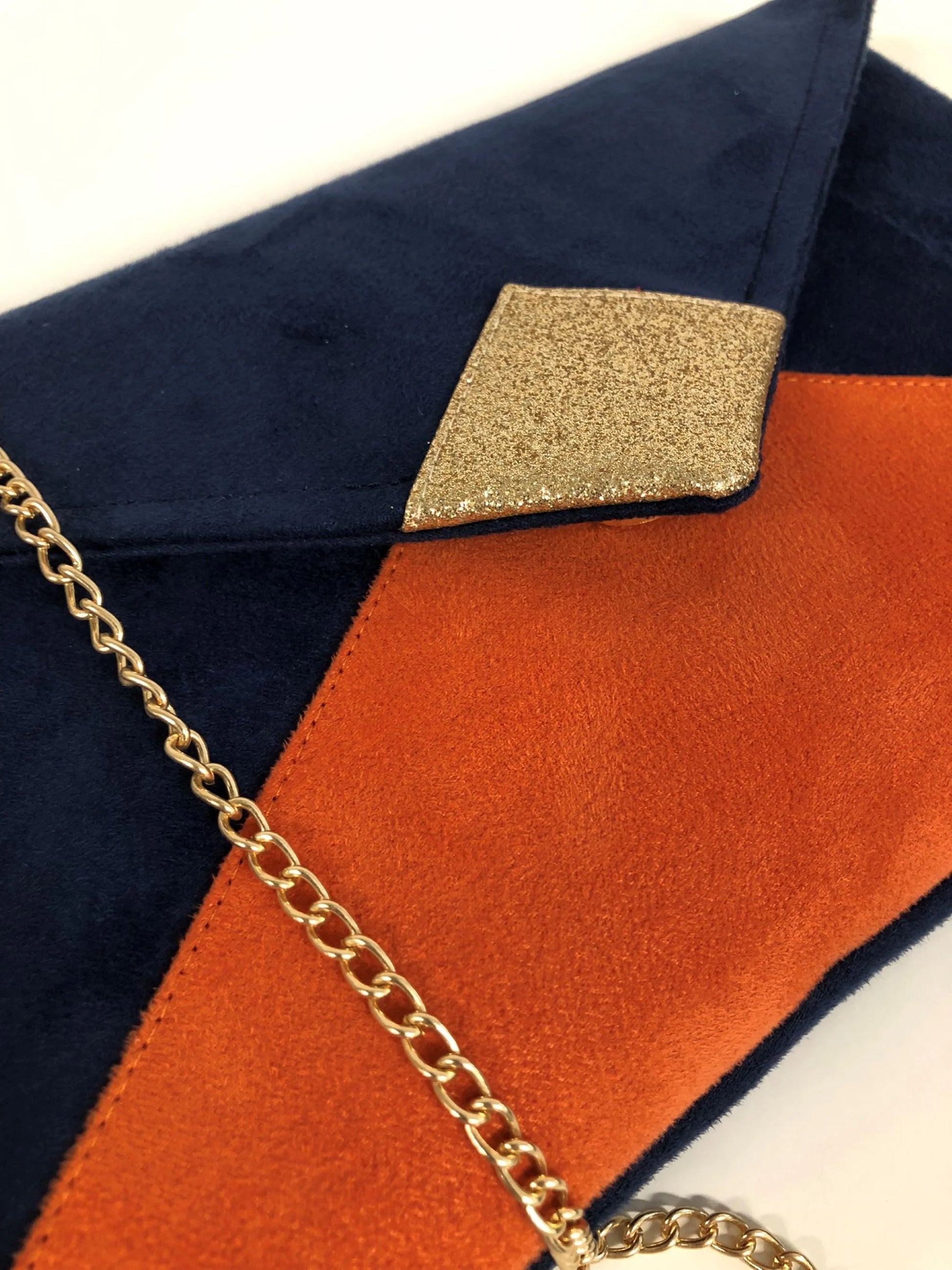Vue détaillée du sac pochette Isa bleu marine et orange à paillettes dorées, avec chainette amovible.